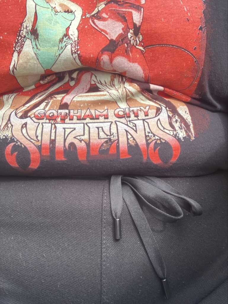 Foto af tyk overkrop med sort t-shirt med illustration af Gotham City Sirens.